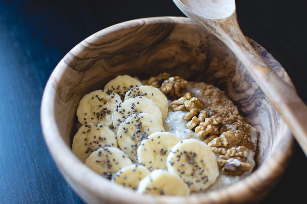 Bowl of oatmeal topped with sliced banana, chia seeds, and walnuts. Oats and bananas are both sources of soluble fiber, which helps firm up stool.